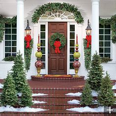 a house decorated for christmas with wreaths on the front door and trees in pots