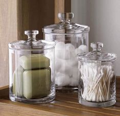 three glass containers filled with candles on top of a wooden table