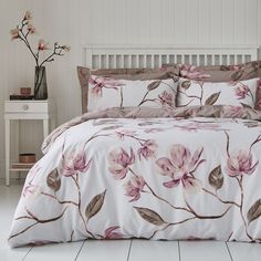 a bed with pink flowers on it in a white and brown bedroom area, next to a night stand