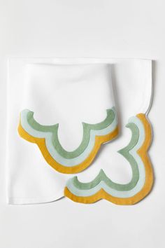 two white napkins with green and yellow designs on the edges, one folded in half