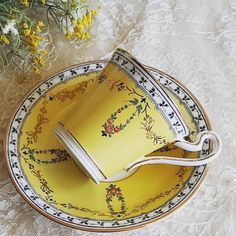 a yellow tea cup and saucer sitting on top of a white lace tablecloth