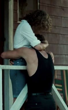 two people standing on the porch of a house with their arms around each other's shoulders