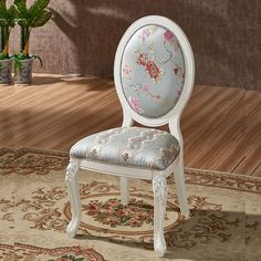 a white chair sitting on top of a rug next to a plant in a vase