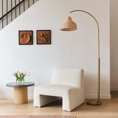 a white chair sitting next to a table with a vase on it and a lamp