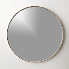 a round mirror on the wall with a gold rim around it and a white background