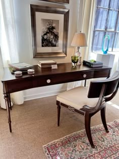 a desk with a lamp and pictures on the wall behind it in front of a window