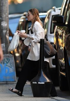 a woman is walking down the street with her purse and coffee cup in her hand