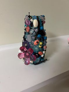 a cell phone covered in lots of different colored beads and stones on a white surface