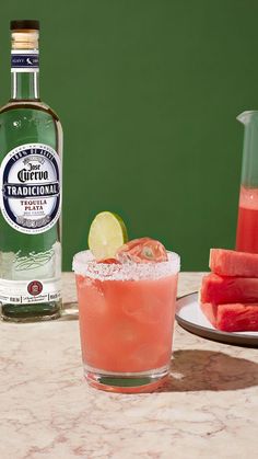 a glass filled with watermelon and lime next to a bottle of alcohol on a table