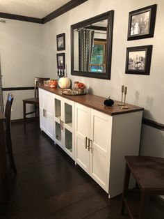 a dining room with white cupboards and wooden flooring next to a mirror on the wall