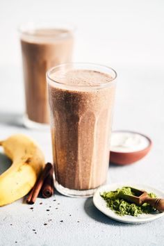 there is a smoothie in a glass next to a banana and cinnamon on the table