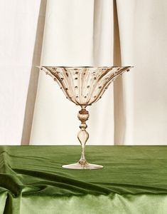 a glass vase sitting on top of a green tablecloth covered table next to a white curtain