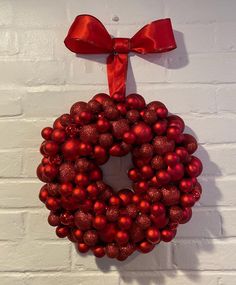 a red christmas ornament hanging on a white brick wall with a red bow