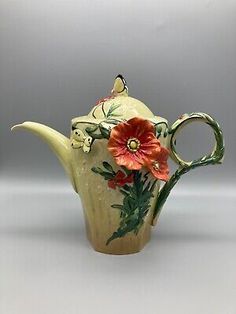 a ceramic tea pot with flowers painted on the side and handle, sitting on a white surface