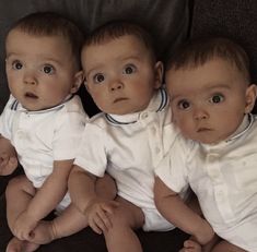 three baby babies sitting next to each other on top of a couch in white shirts