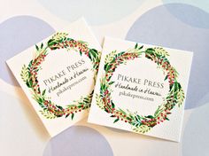 two business cards with watercolor wreaths on them sitting on a polka dot background