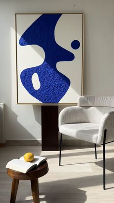 a white chair sitting in front of a blue and white painting on a wall next to a table