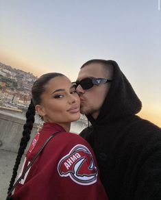 a man and woman kissing each other in front of the ocean with buildings behind them