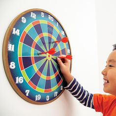 a young boy is playing with a colorful dart on a wall mounted bulls eye clock