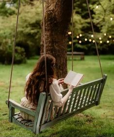 a woman sitting on a swing reading a book