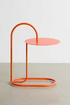 an orange table sitting on top of a cement floor next to a white wall and a round metal object