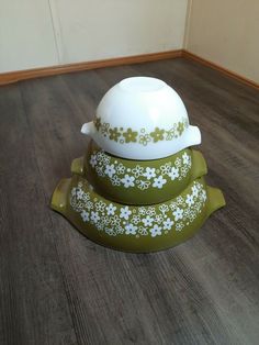 three green and white dishes stacked on top of each other in a room with wood flooring