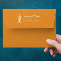 a hand holding an orange envelope with a cactus on the front, and a blue background