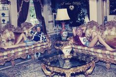 two women sitting on couches in a living room with chandelier and lamps