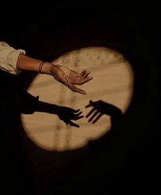 two hands reaching out towards each other in front of a circular shadow on the ground