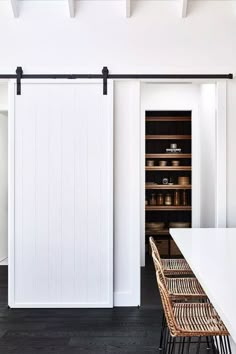 a kitchen with white walls and black flooring next to an open closet door that has sliding doors on both sides