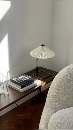 a white chair sitting next to a table with a book on it and a lamp