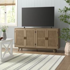 a living room with a large television on top of a wooden entertainment center in front of a window