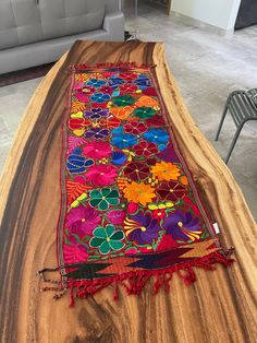 the table is made out of wood and has colorful flowers on it, along with a red tassel