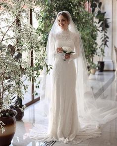 a woman in a white wedding dress standing next to a tree and potted plant