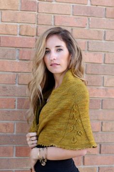 a woman standing in front of a brick wall wearing a yellow sweater and black skirt