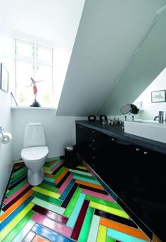 a white toilet sitting under a window next to a sink in a room with multicolored flooring