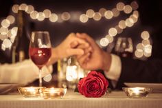 two people holding hands at a table with wine glasses and candles in front of them