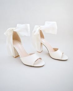 a pair of white high heeled shoes with a bow