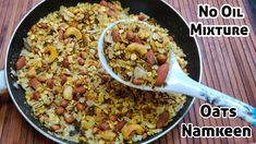 a pan filled with lots of food sitting on top of a wooden table next to a spoon