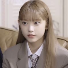 a young woman with long hair wearing a suit and tie sitting on a brown couch