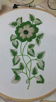 a close up of a embroidery on a white cloth with green leaves and flowers in the center