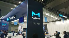 a group of people standing around a booth at a trade show with marbell logo on the wall