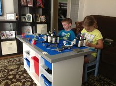 two children play with legos on a table in the living room, while another child watches