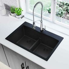 a kitchen sink with two black sinks and a green plant in the window sill