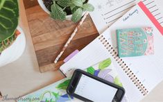 a wooden table topped with notebooks next to a potted plant and cell phone