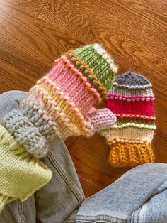 two knitted hats sitting on the floor next to someone's jeans and shoes