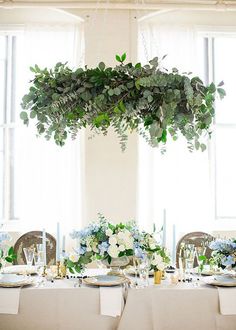 the table is set with white linens and greenery hanging from it's ceiling