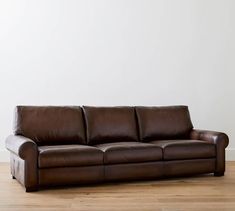 a brown leather couch sitting on top of a hard wood floor next to a white wall