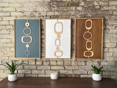 three framed art pieces on a brick wall above a wooden table with two potted plants