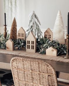 a wicker table topped with wooden houses and greenery next to candlesticks